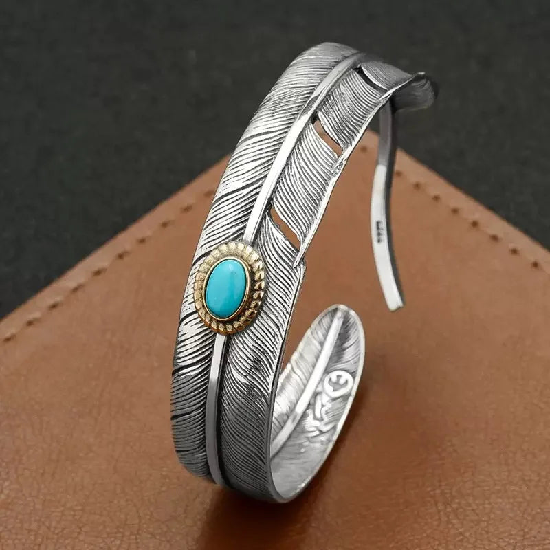 Antiqued silver feather cuff with an oval turquoise stone, angled view